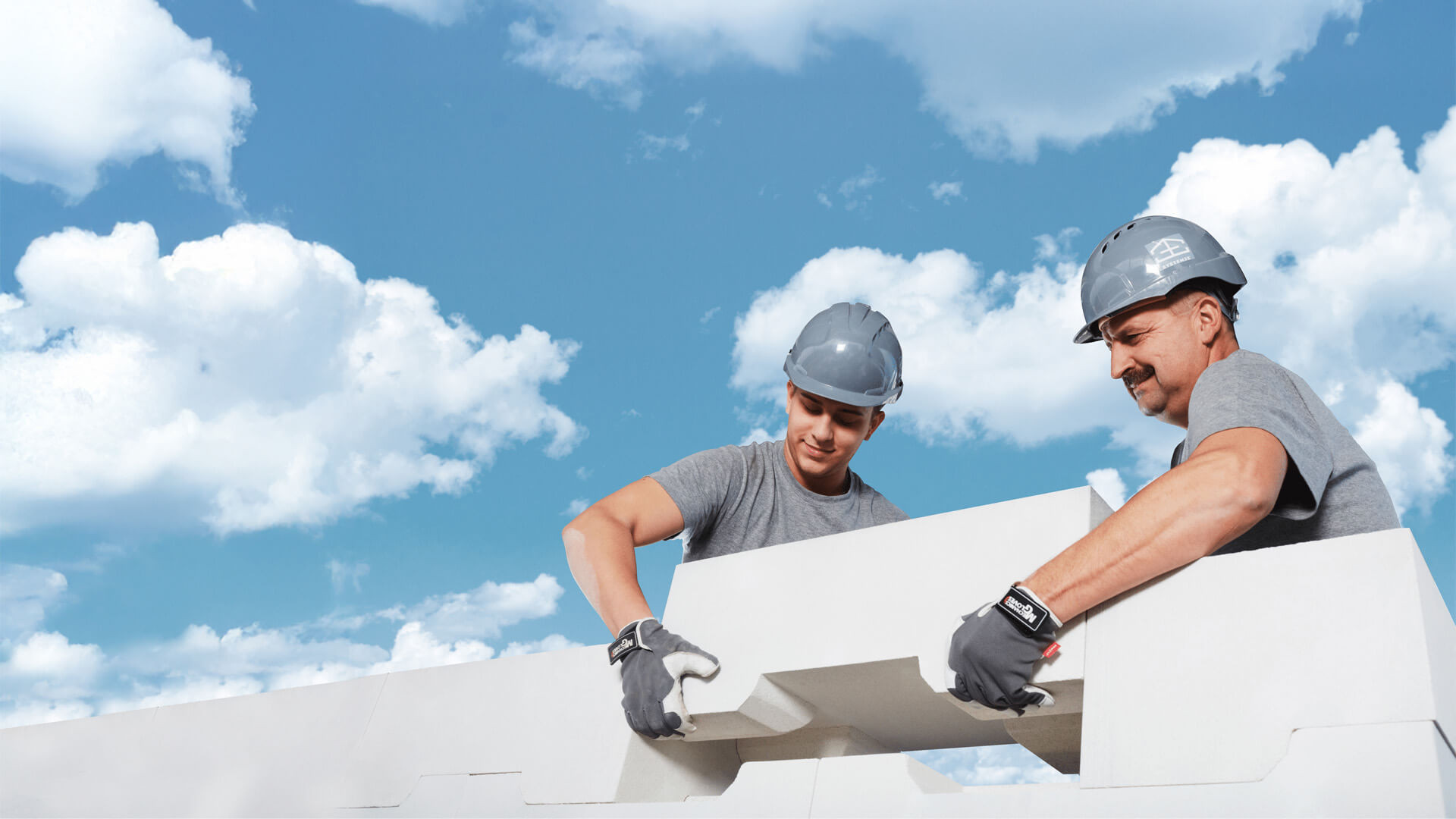 Two builders dry-stacking an interlocking mineral block of System3E, no mortar